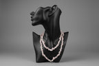 Black mannequin head with a pink beaded rose quartz necklace on a gray studio background