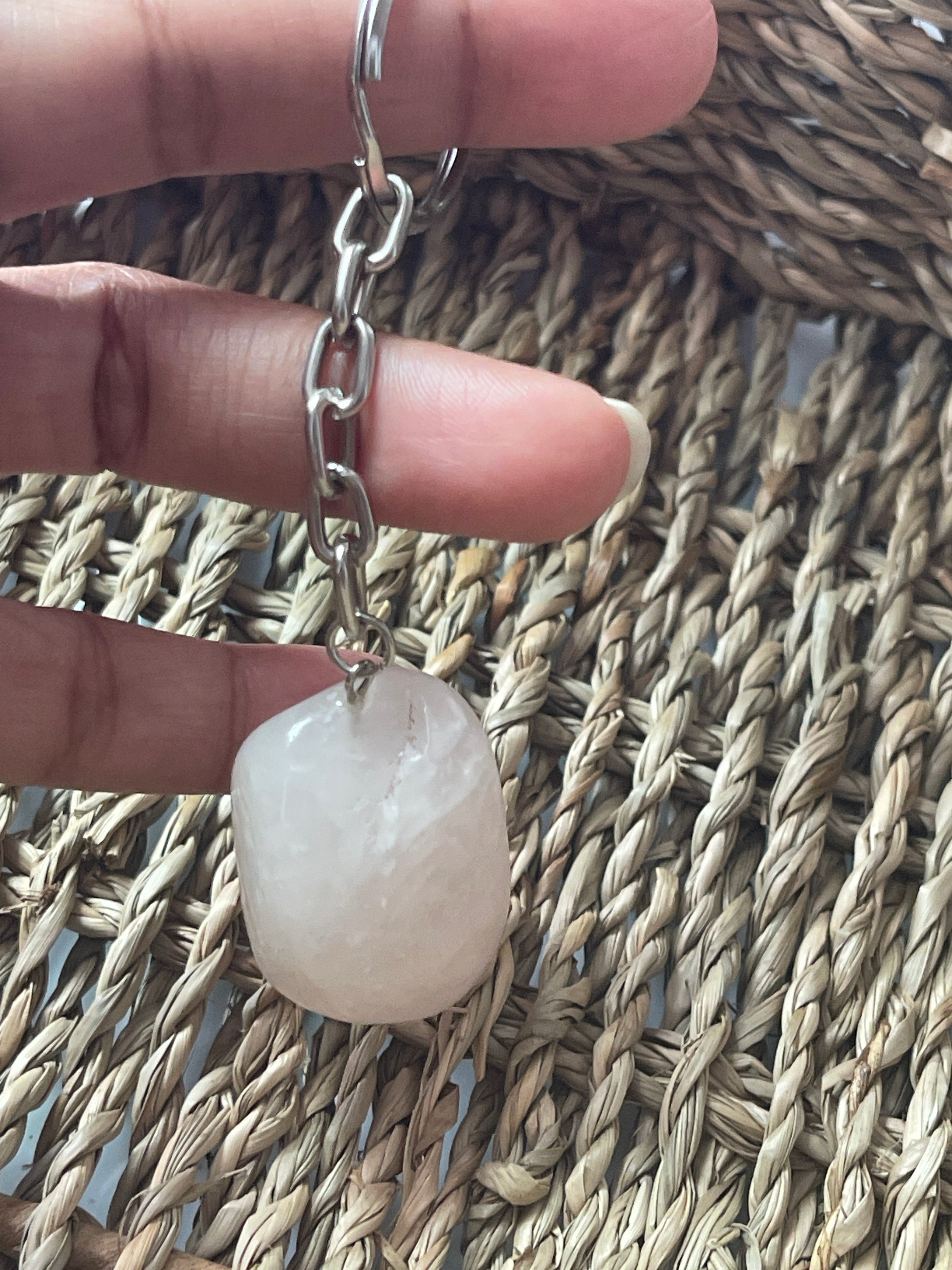 Hand holding a rose quartz keychain with a pink stone against a woven mat background