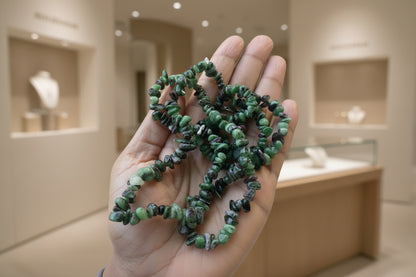 Hand holding a string of small green Ruby_Zoisite_Necklace_30-32_Inches with a blurred outdoor background
