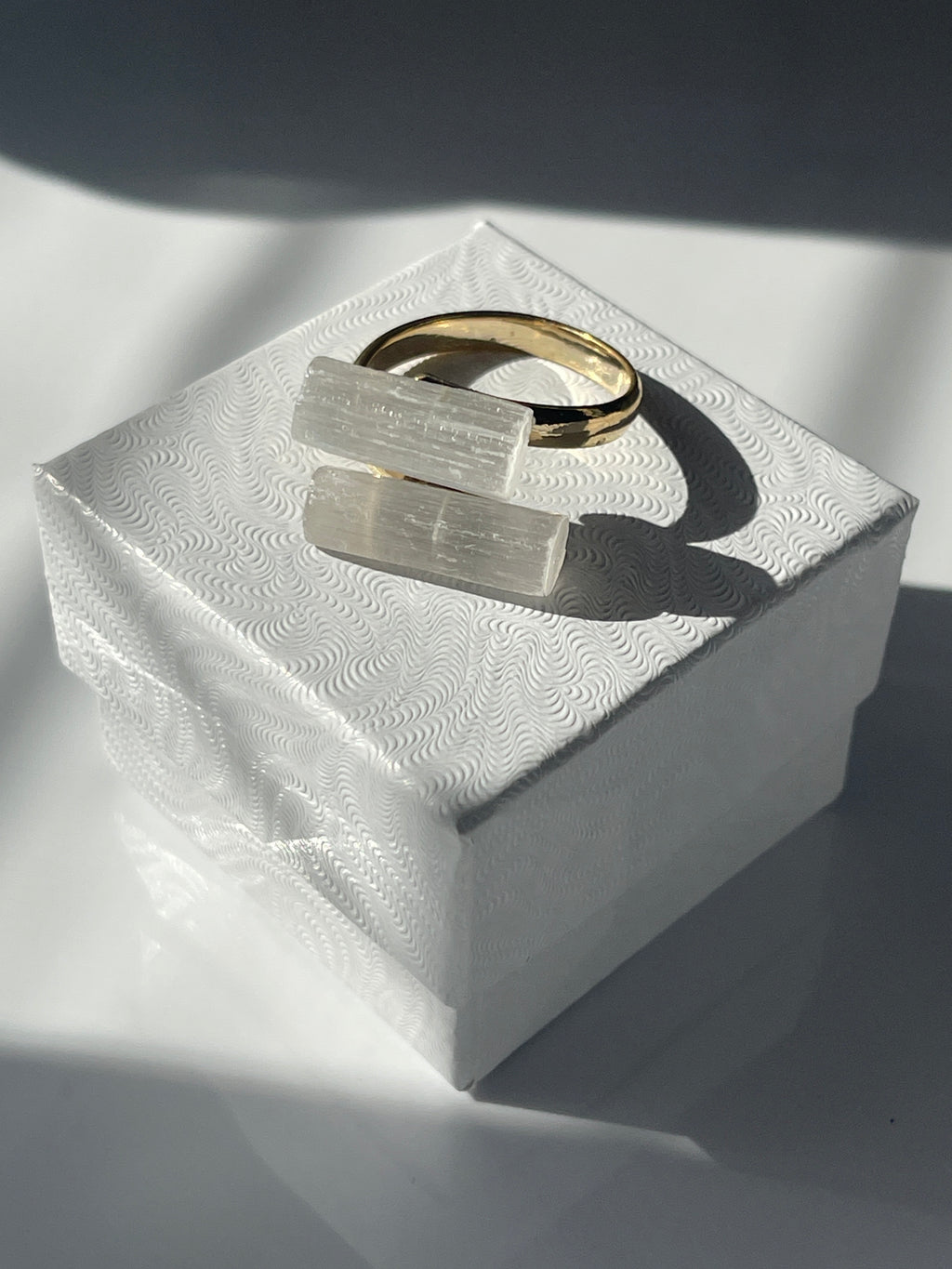 Selenite gold plated ring on a white jewelry box a textured white surface