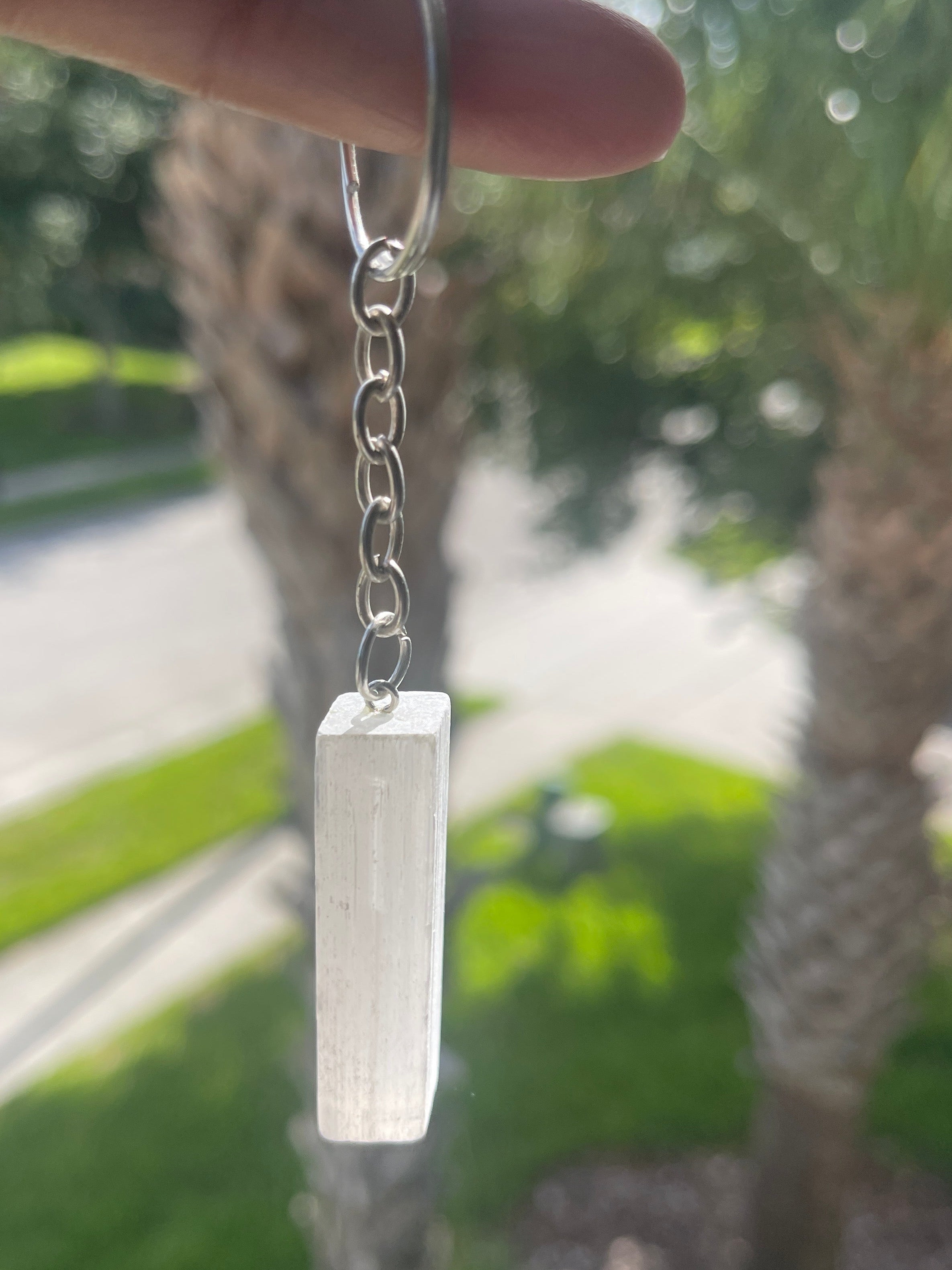 Hand holding a Selenite Keychain silver keychain with a rectangular silver charm against a blurred outdoor background