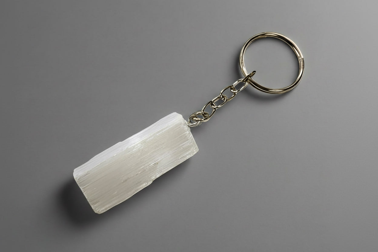 A rough selenite keychain with a silver-colored metal ring and chain, against a green background.