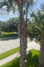 Person outside by Palm tree holding Tera necklace, a street with trees and houses in the background.