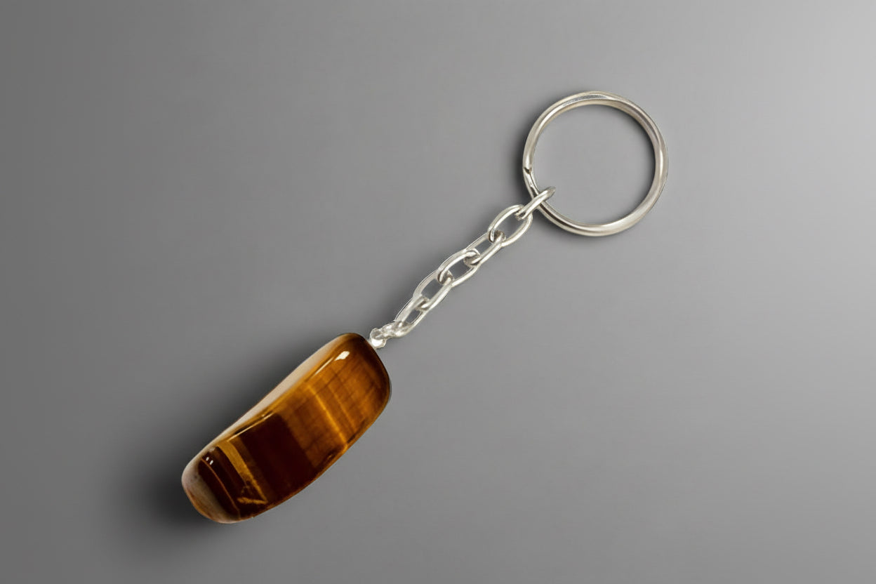 A polished keychain with a Tiger's Eye stone set on a metal ring, against a gray  background.
