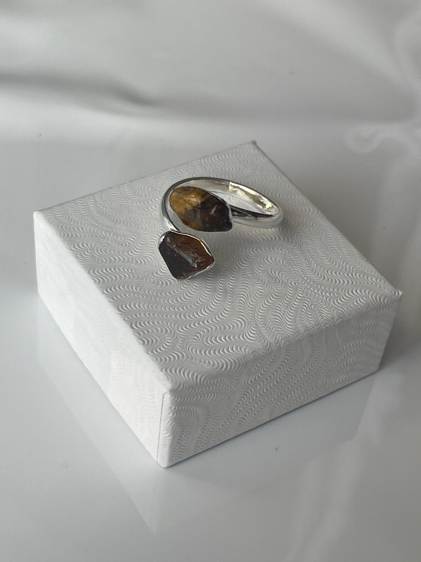 Tigers eye sliver plated ring, brown stone on a textured white jewelry box top against a white background