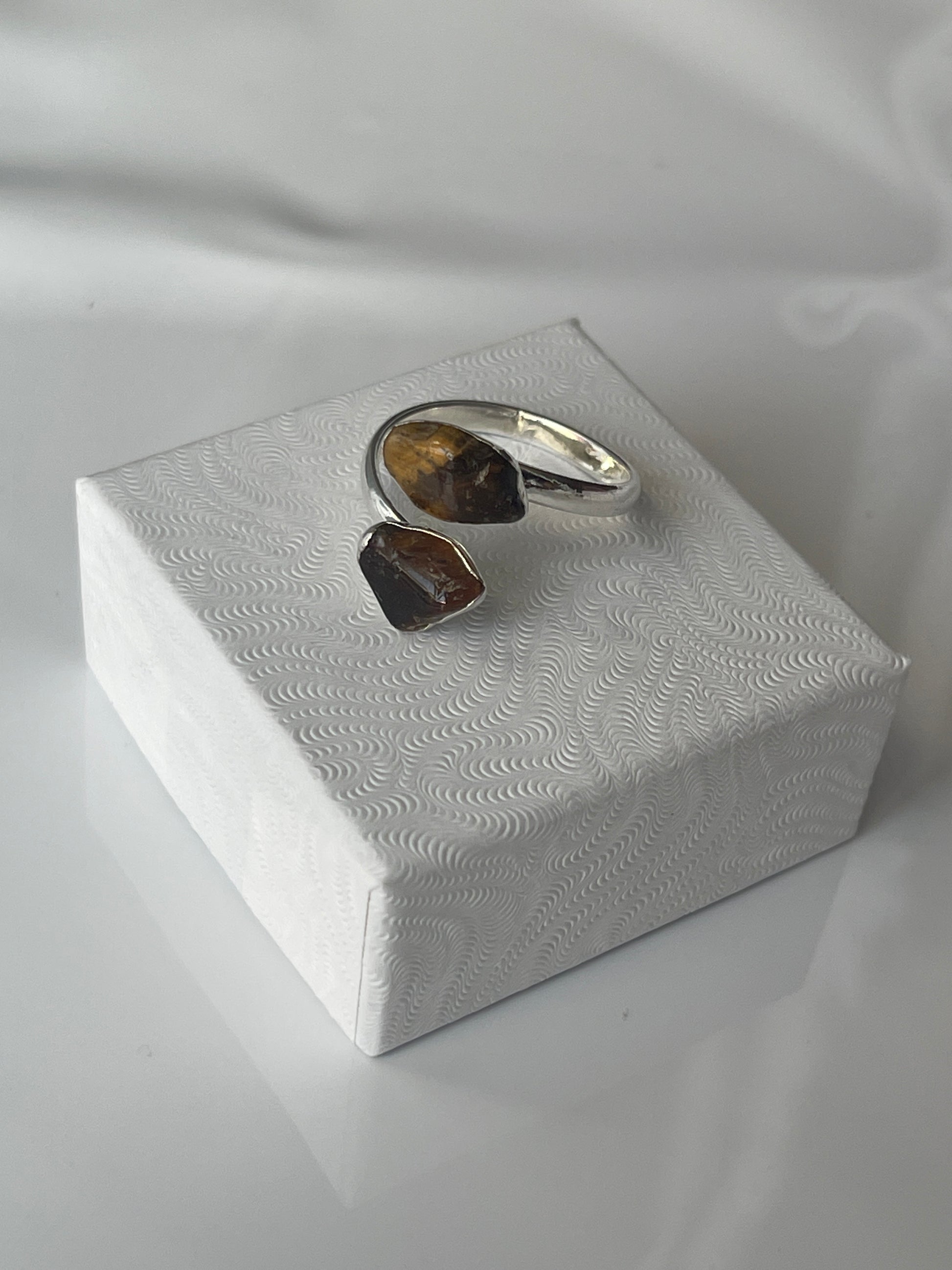 Tigers eye sliver plated ring, brown stone on a textured white jewelry box top against a white background