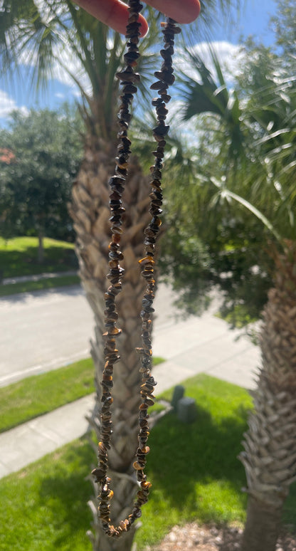 Tigers_Eye_Chip_Necklace_30-32_Inches with black beads held up to palm trees