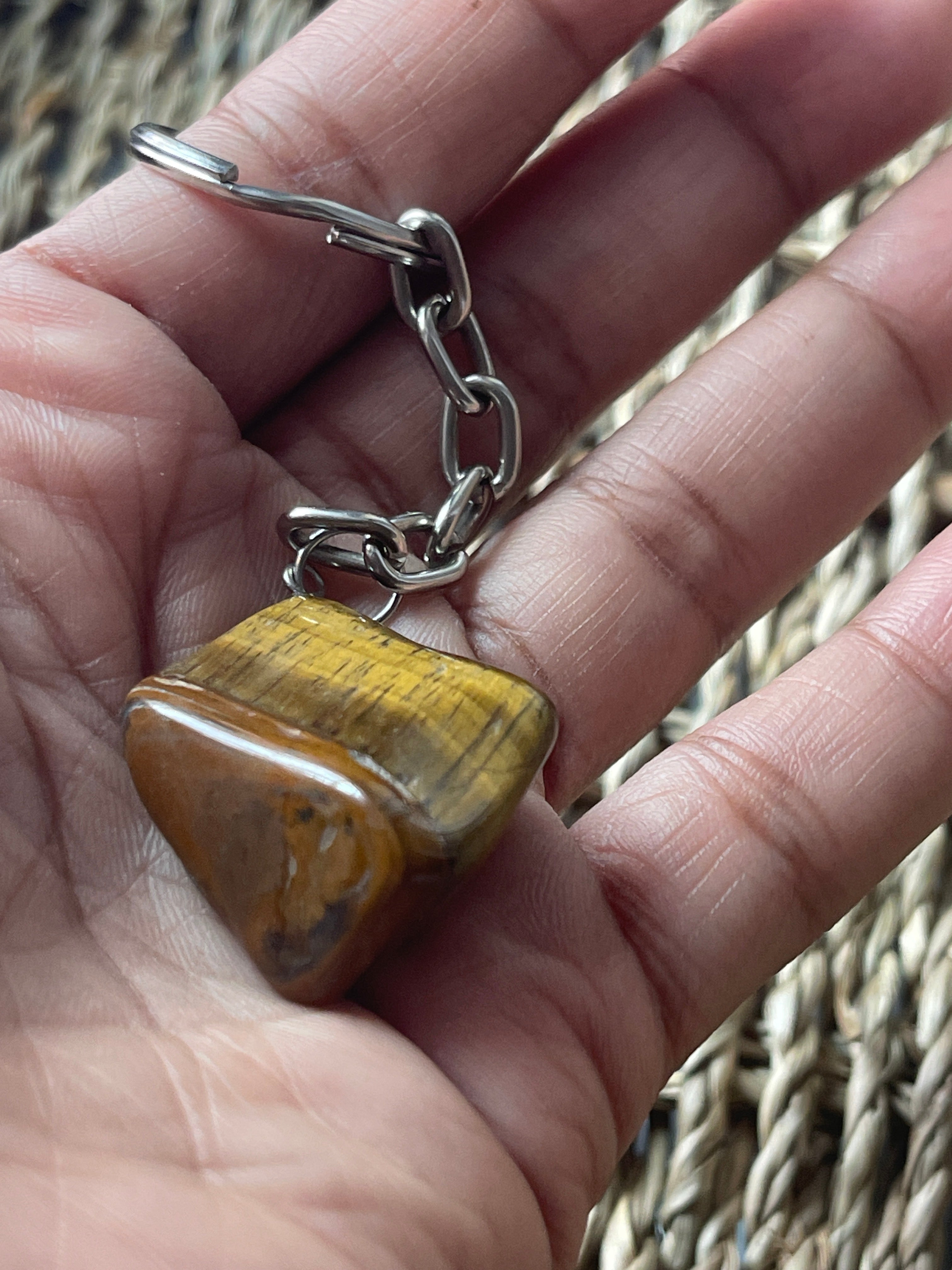 Hand holding a keychain with a yellow tiger's eye stone against a woven background