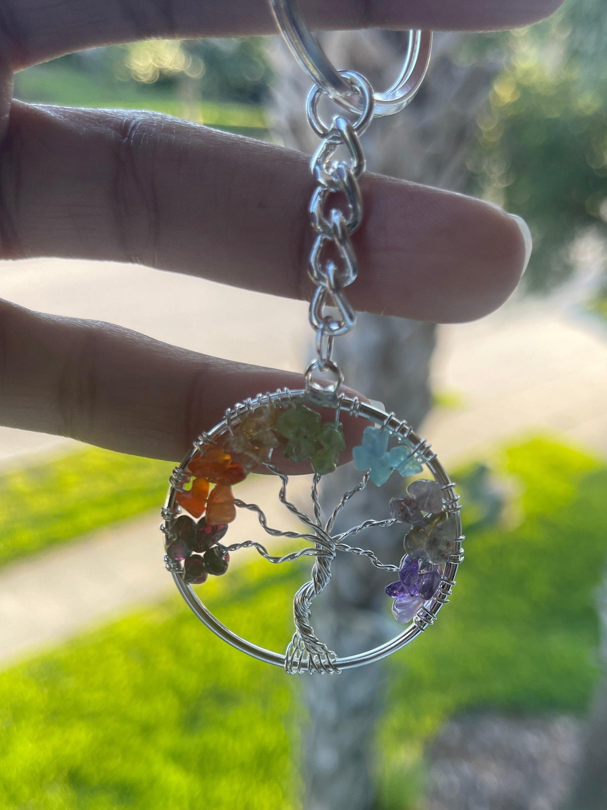 Hand holding a Tree of Life Keychain with a tree of life design outdoors