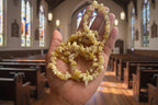 Hand holding a Yellow_Opal_Necklace_30-32_Inches, yellowish beads against a blurred church background