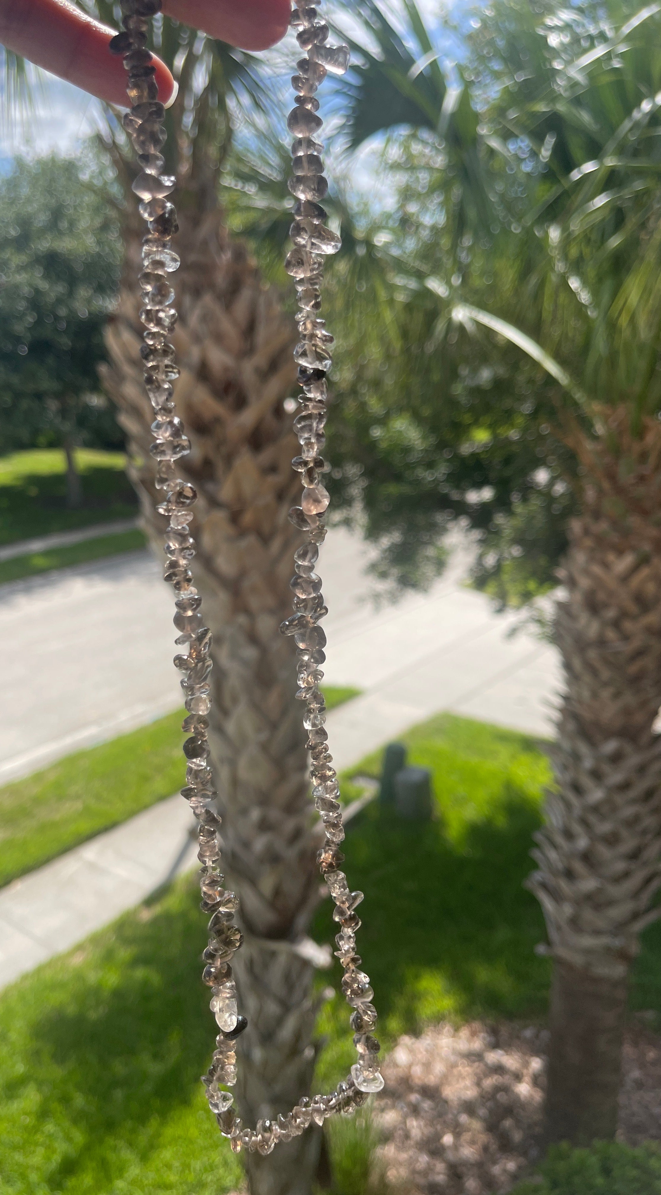 Close-up of a smoky-quartz-necklaces-30-32-inches with crystals against a blurred outdoor background