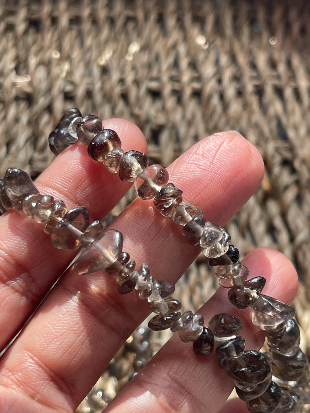 Hand holding a string of smoky quartz necklace 30-32 inches in Florida, faceted beads against a textured woven background