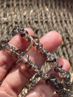 Hand holding a string of smoky quartz necklace 30-32 inches in Florida, faceted beads against a textured woven background