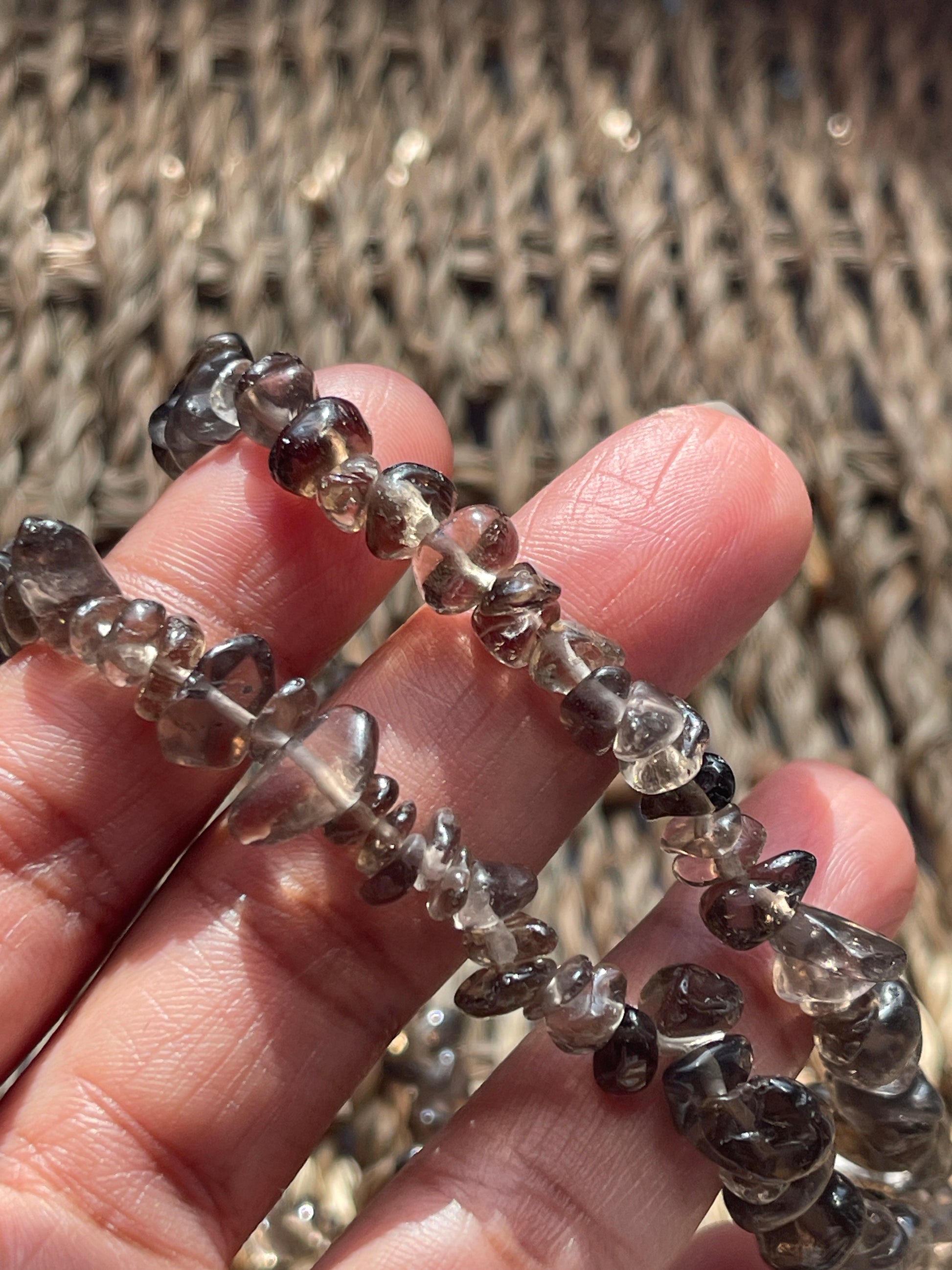 Hand holding a string of smoky quartz necklace 30-32 inches in Florida, faceted beads against a textured woven background