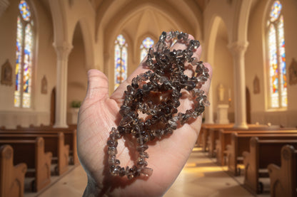 Hand holding smoky-quartz-necklaces-30-32-inches brown beads against a blurred chapel background